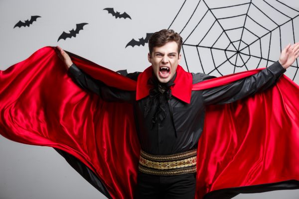 homem utilizando a ideia de fantasia para halloween de caracterização como vampiro, com para preta de verso vermelho e dentes muito afiados. 